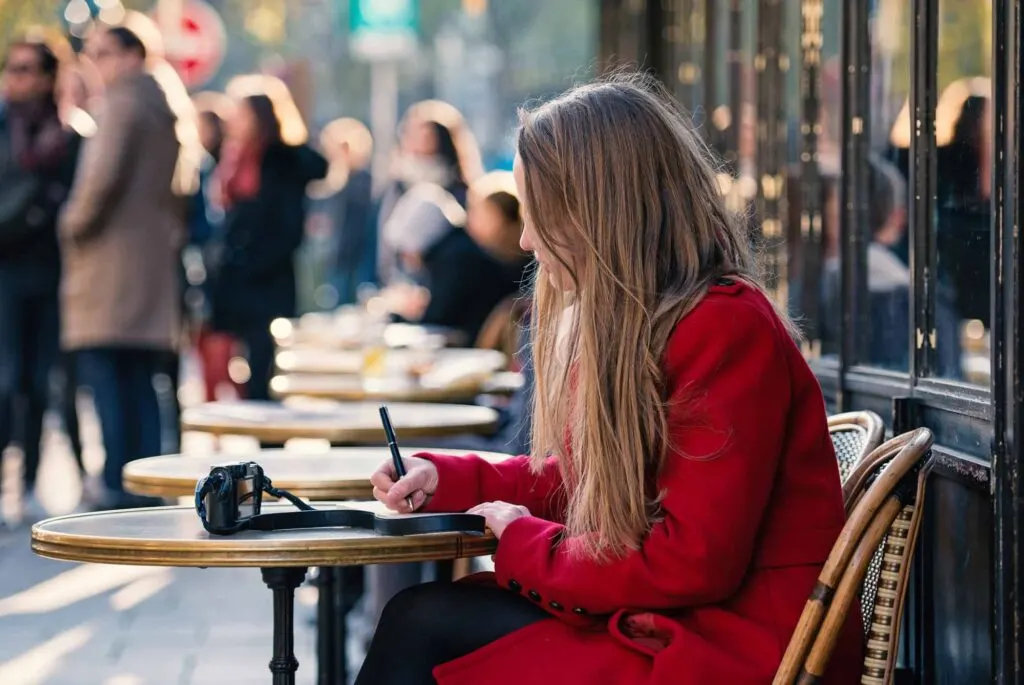 Young blonde woman portrait sit in a typical coffee shop in the city writing on a notebook in Paris