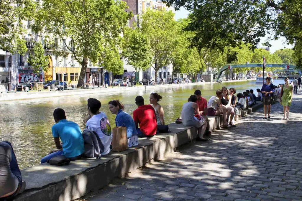 People hang out by Canal Saint Martin under trees in Paris