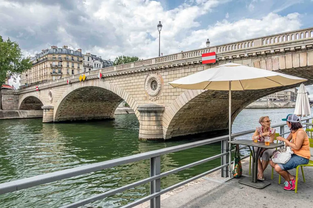 Two women drink a beer at a table by the Seine riverbank