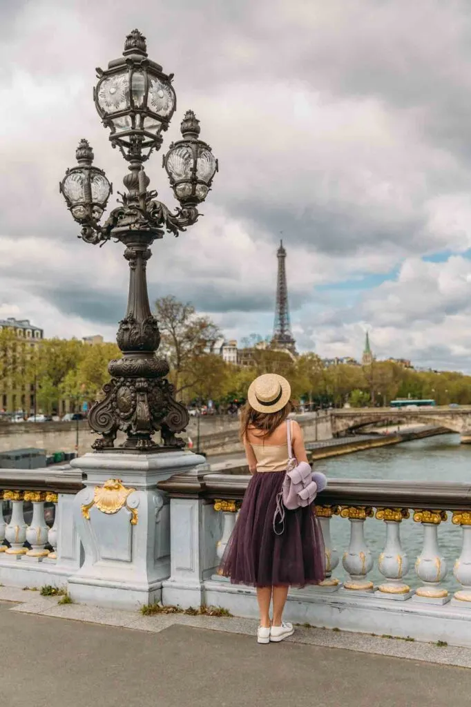 Pretty faceless girl in skirt and hat admiring the view from pont Alexandre III to Eiffel Tower