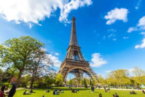 Eiffel Tower on a sunny day while people picnic on the Champ de Mars