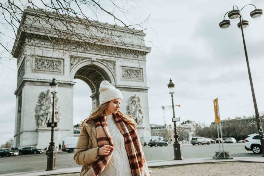 Young fashionable woman wearing winter clothes in front of Arc de Triomphe