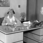 The Legendary Coco Chanel sitting behind a desk