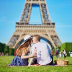 Romantic couple having picnic on Champs de Mars with wine and fruits with the Eiffel tower in the background