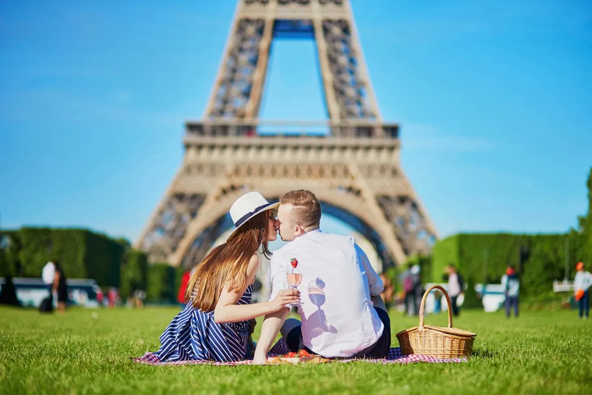 Romantic couple having picnic on Champs de Mars with wine and fruits with the Eiffel tower in the background