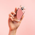 A woman's hand elegantly holds a glass of a French perfume brand